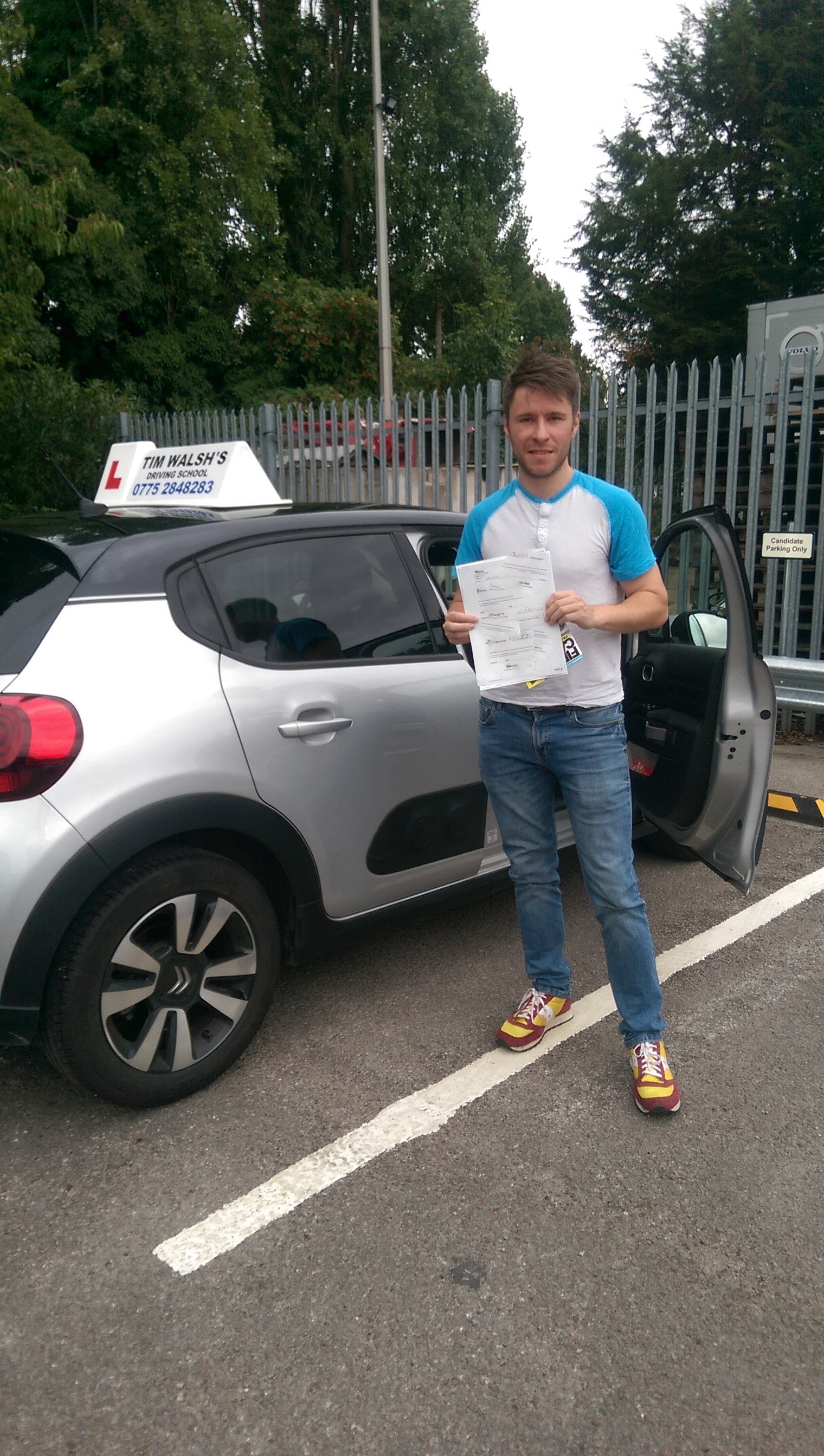 Past student Ben holding his test certificate next to the instructor car