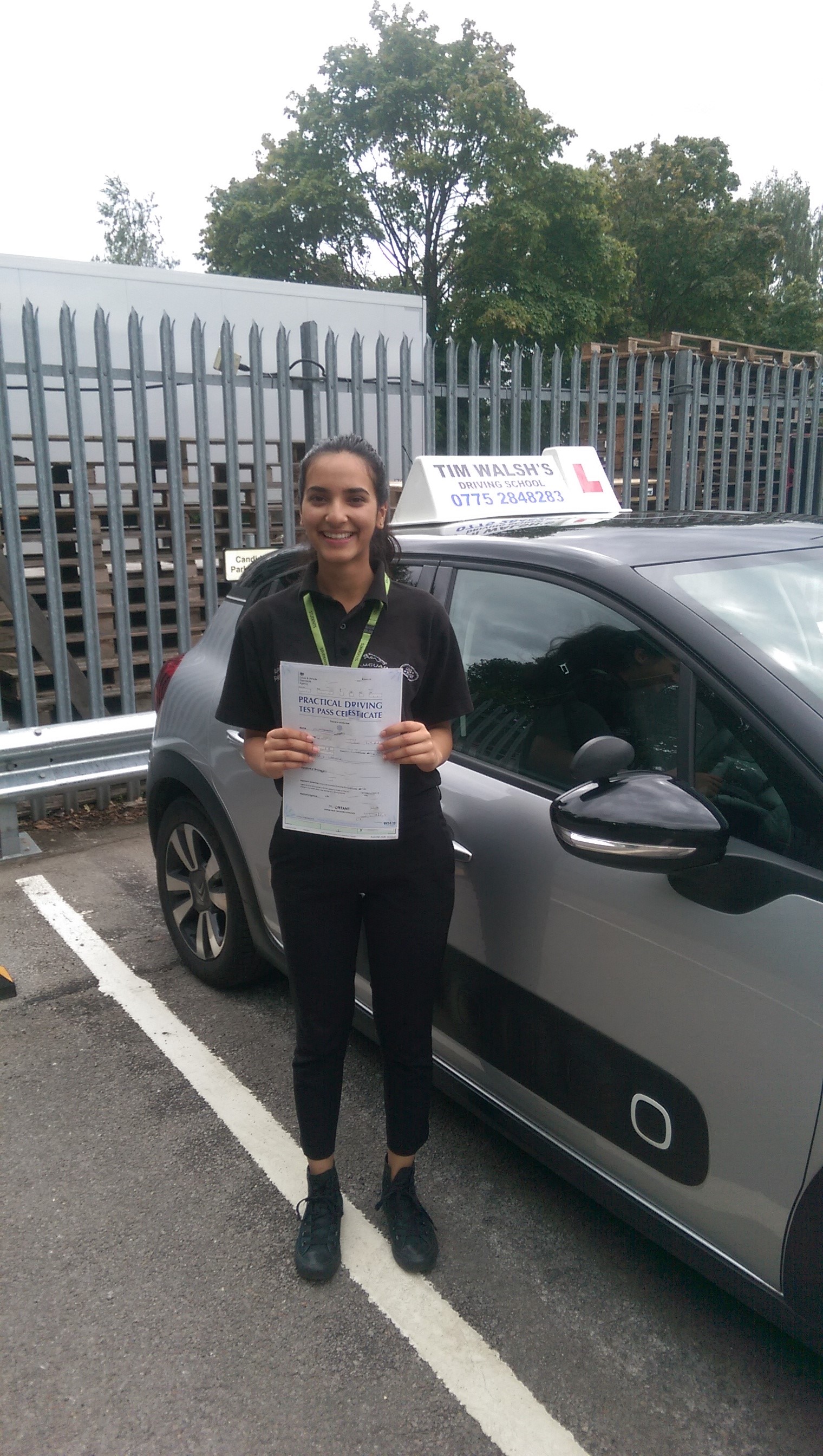 Past student Jemma holding her test certificate next to the instructor car