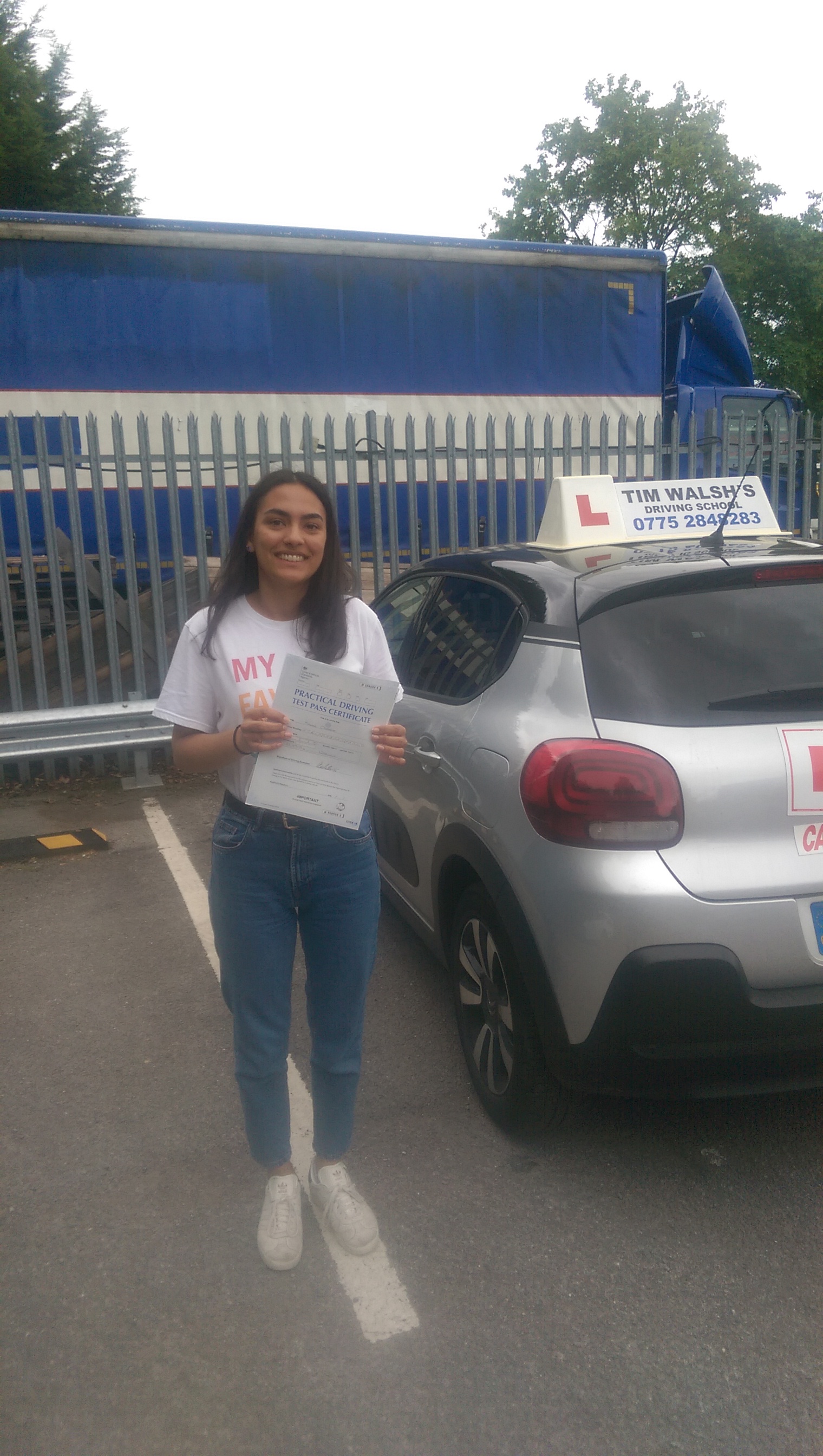 Past student Maxine holding her test certificate next to the instructor car