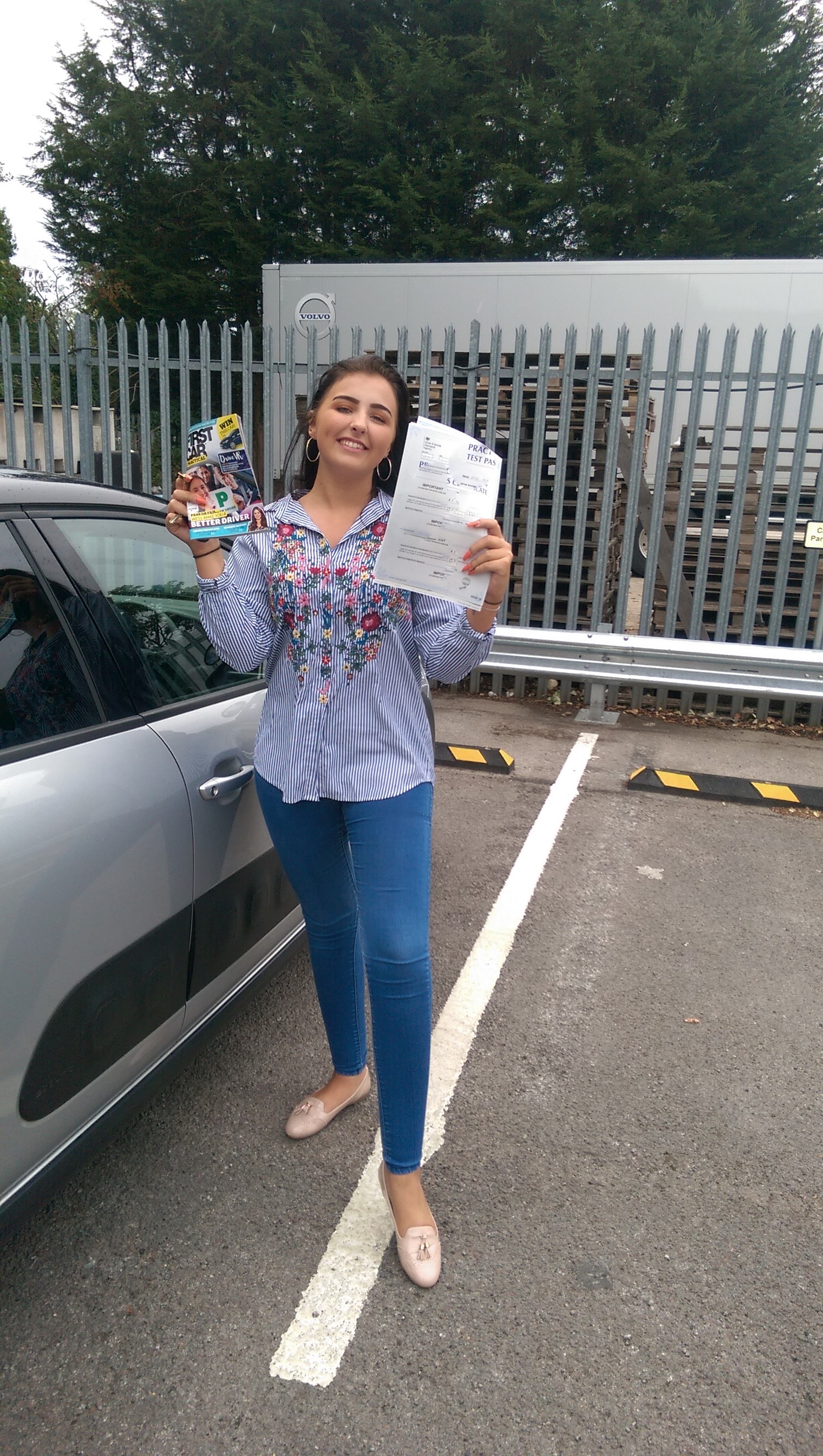 Past student Mia holding her test certificate next to the instructor car